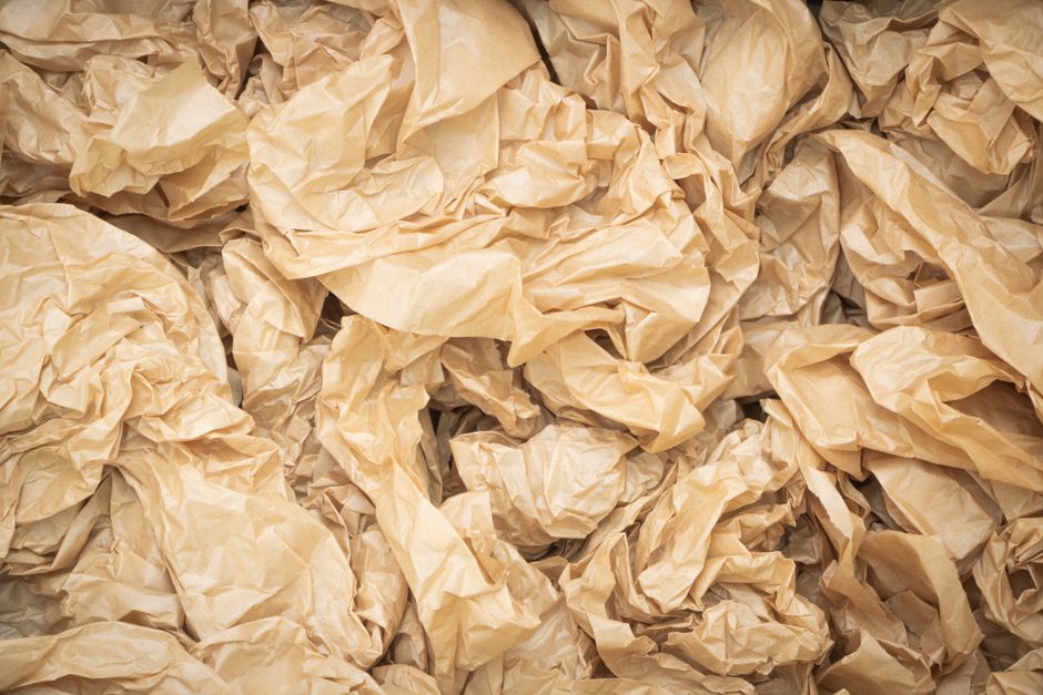 A close-up image of numerous crumpled brown paper bags piled together on a flat surface. The paper bags vary in size and have a textured, wrinkled appearance, with some edges slightly torn. There are